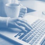 Person using a laptop while holding a coffee mug.