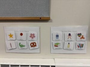 Two laminated charts on a wall showing coping strategies for children. The left chart is titled ‘My Deep Breath Choices’ and includes six illustrated options: STAR, Balloon, Flower, Candle, Dinosaur, and Pretzel. The right chart is titled ‘My Calm Down Choices’ and includes six illustrated options: Drink Water, Take a Walk, Fidget, Read a Book, Crunchy Cream, and Color a Picture.