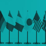 Row of small tabletop flags from several countries arranged side by side against a teal background.