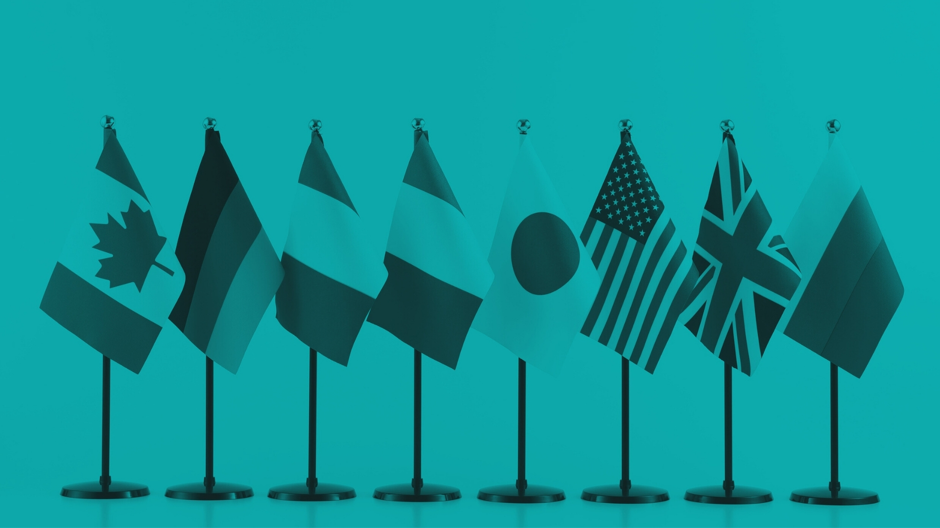 Row of small tabletop flags from several countries arranged side by side against a teal background.