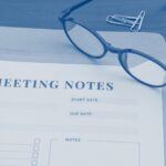 Meeting notes form on a desk with a pen, eyeglasses, and notebook