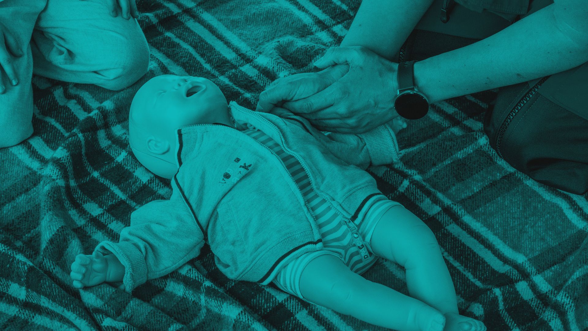 Hands performing CPR compressions on an infant training manikin.
