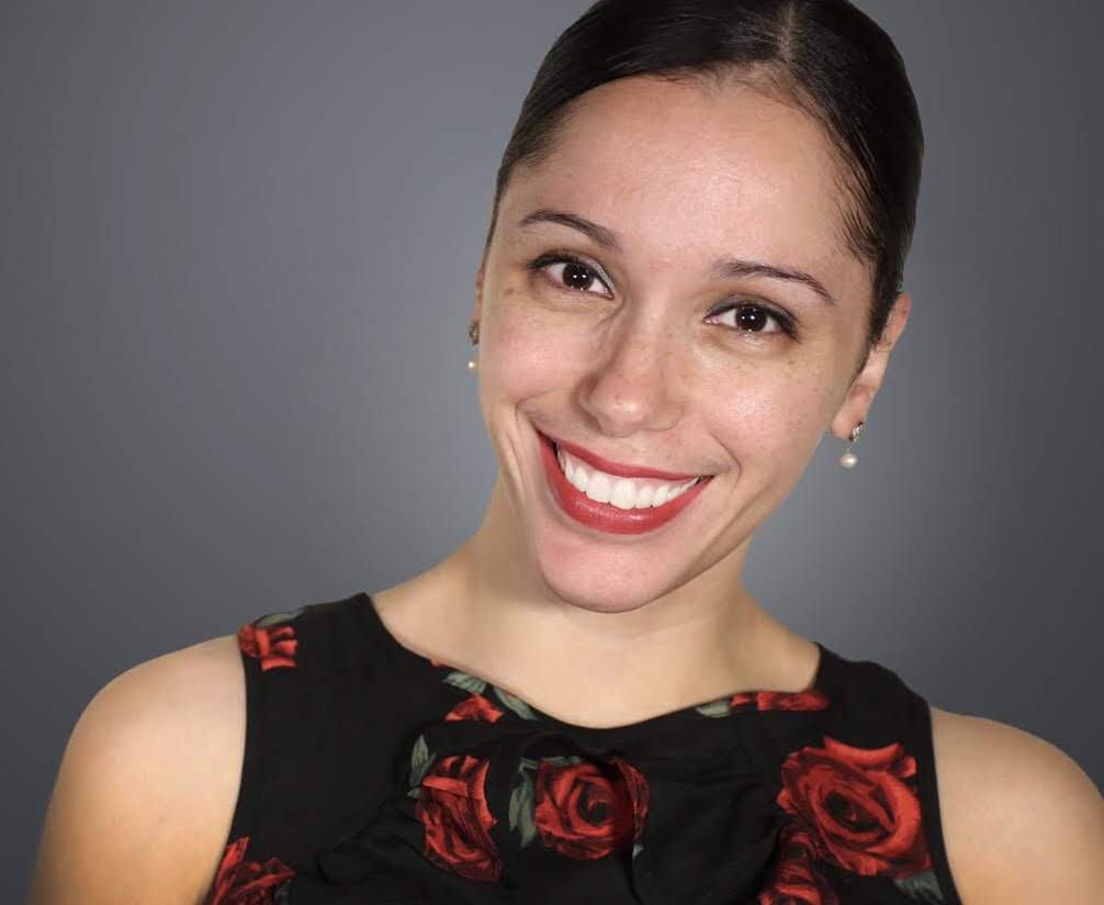 Person wearing a sleeveless black top with a red rose pattern, posed against a dark gray background.