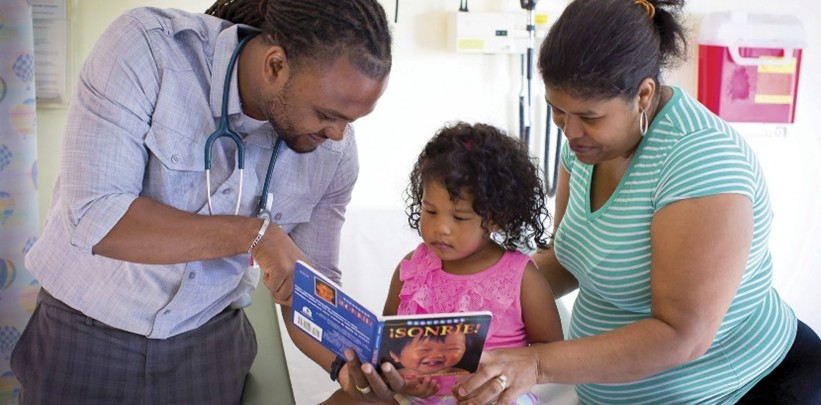 A healthcare provider showing a book to a child seated between two adults during a medical visit.