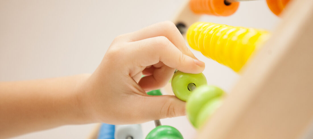 Hand moving a green bead on a colorful wooden abacus.