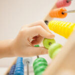 Hand moving a green bead on a colorful wooden abacus.