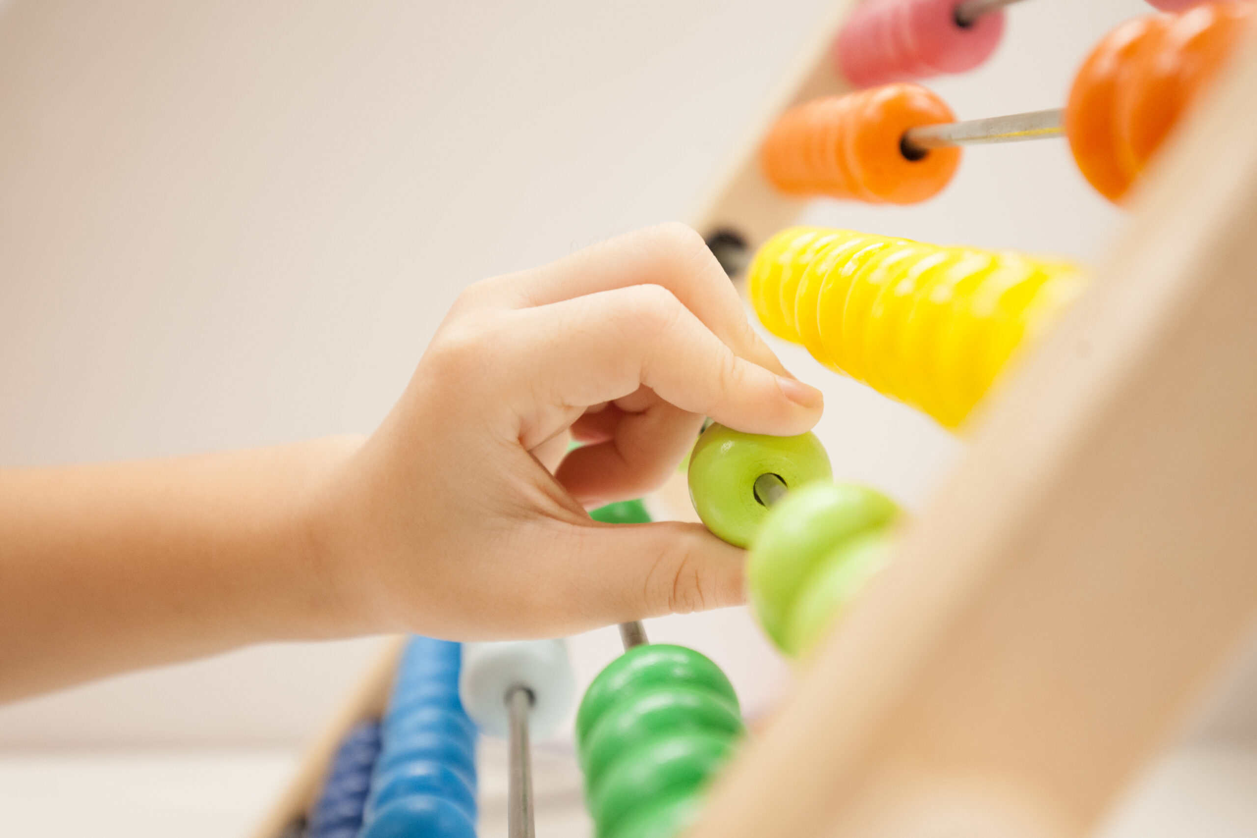 Hand moving a green bead on a colorful wooden abacus.