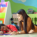 Adult and child lying on the floor reading a book together in a colorful early‑learning classroom.