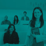 Teal‑filtered image of a student standing in a tiered classroom holding a book, with other students seated in the background.