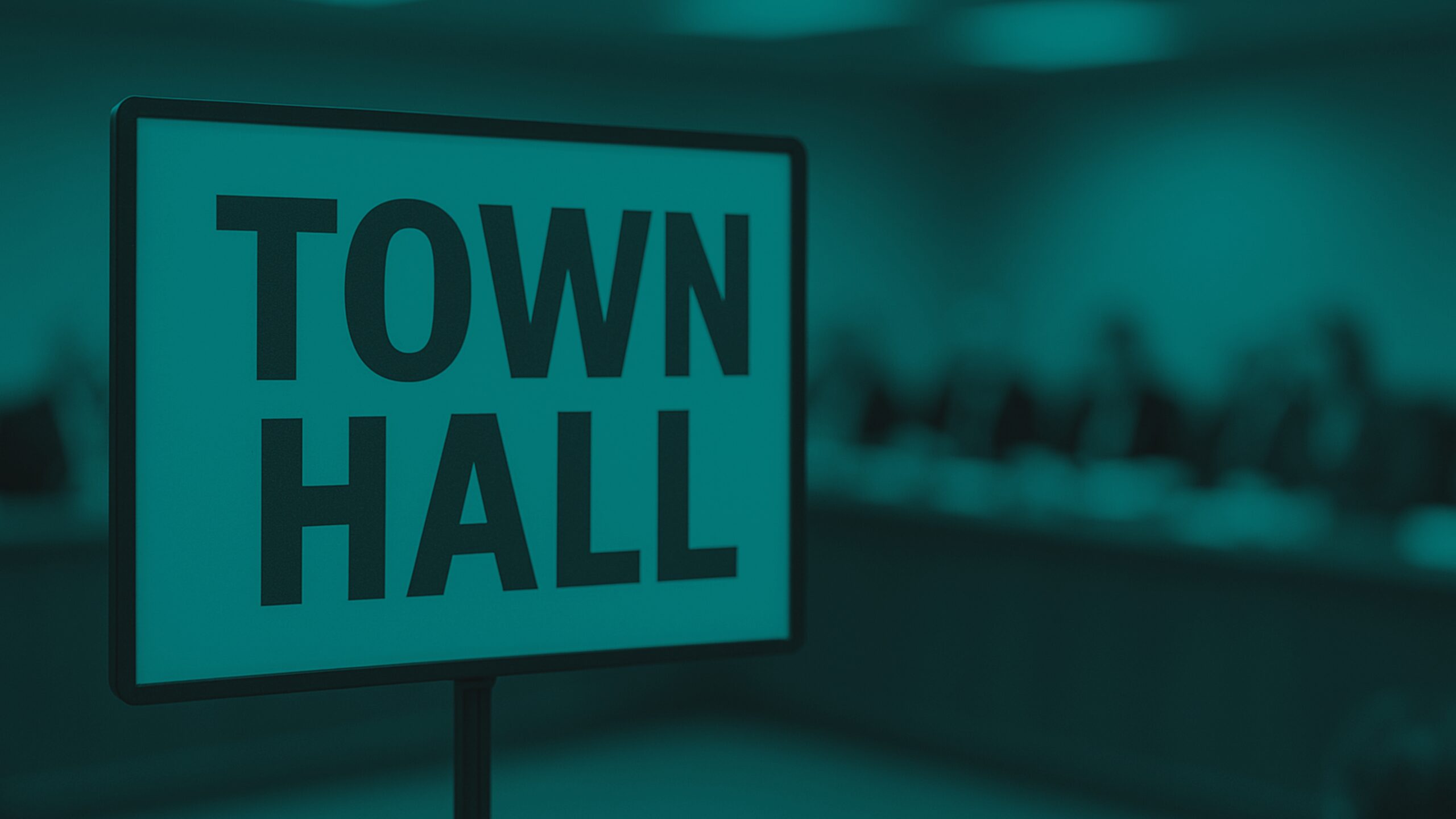 Town hall sign in the foreground with a blurred meeting table and seated council members in the background.