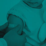 Healthcare worker applying a bandage to a young child’s upper arm after a vaccination, while the child holds a stuffed teddy bear.
