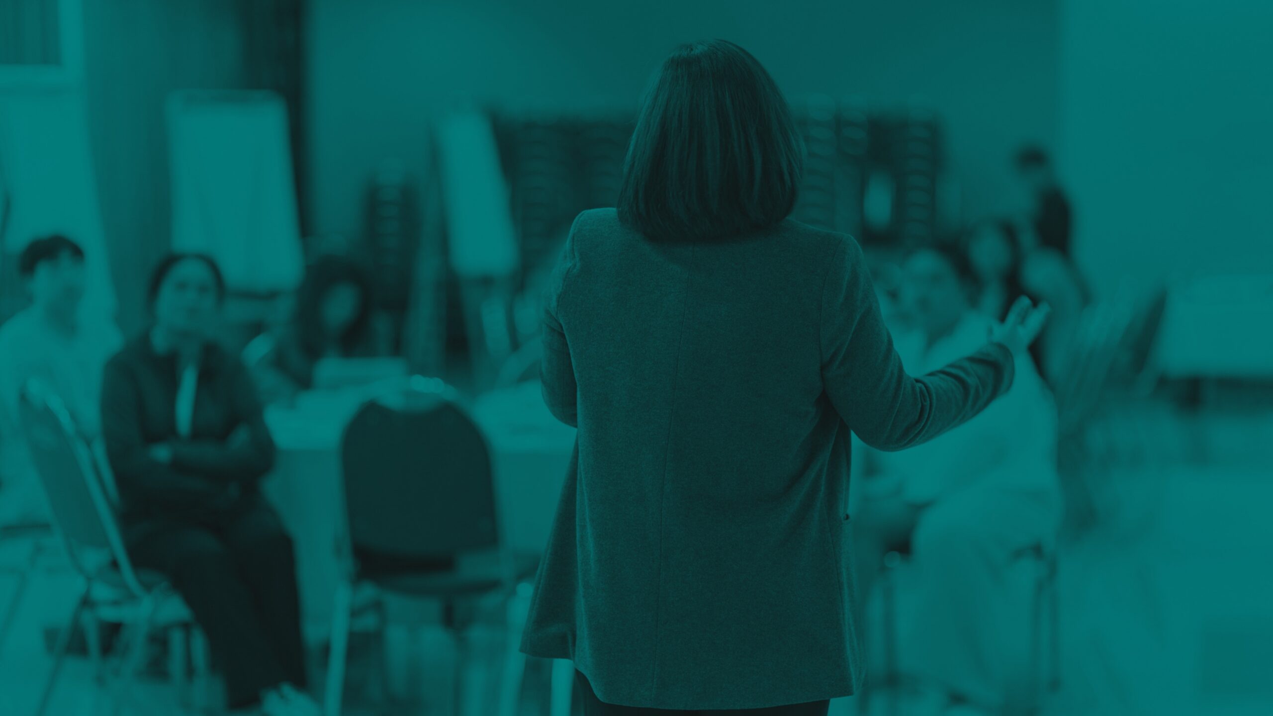 Person speaking to a group seated in a meeting or classroom setting.