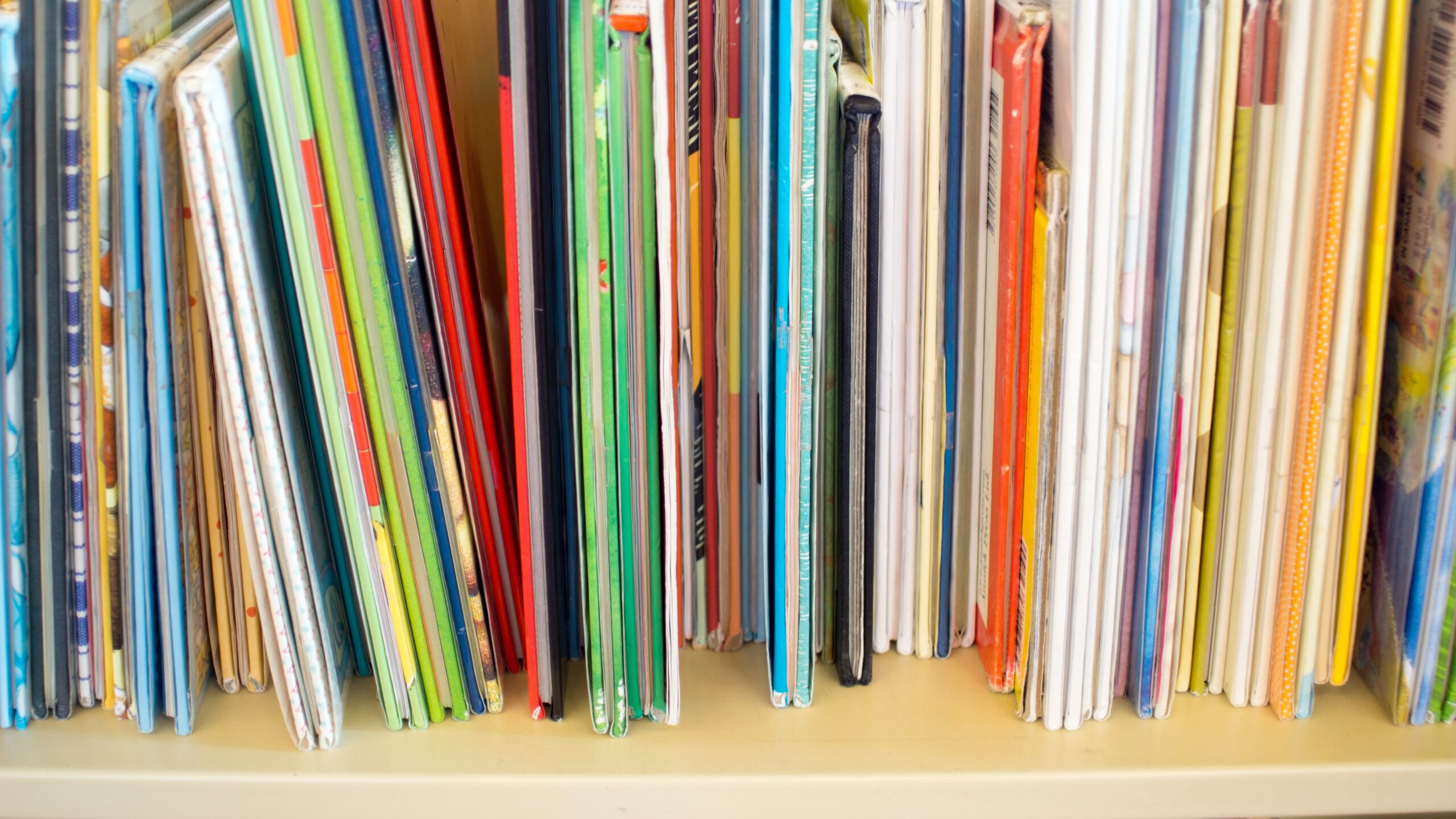 Close-up of colorful children's books lined up on a library or classroom bookshelf.