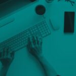 Hands typing on a computer keyboard at a desk with a monitor, phone, and coffee cup.