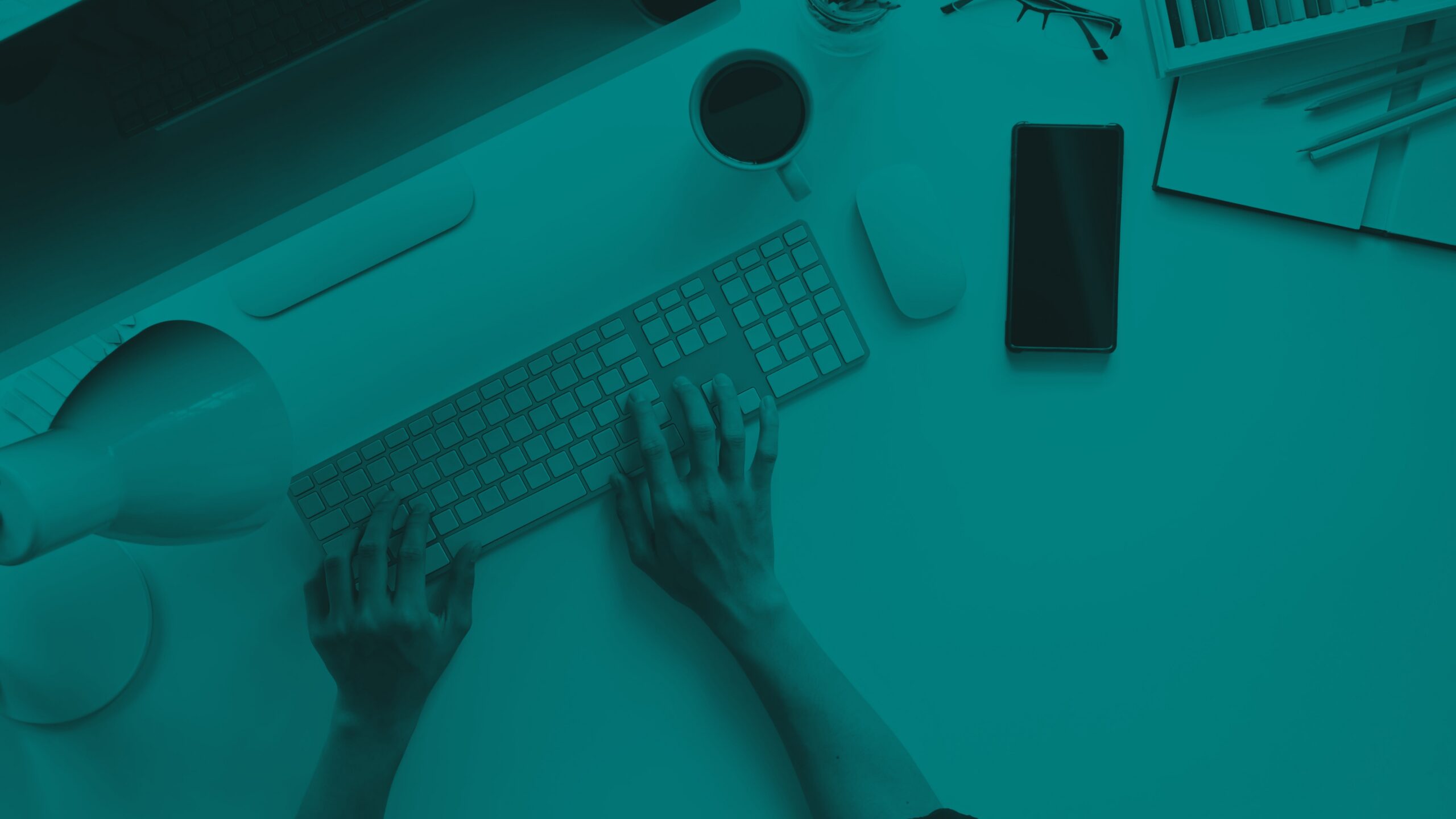 Hands typing on a computer keyboard at a desk with a monitor, phone, and coffee cup.