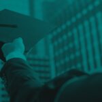 Person holding a graduation cap overhead with a large building in the background.