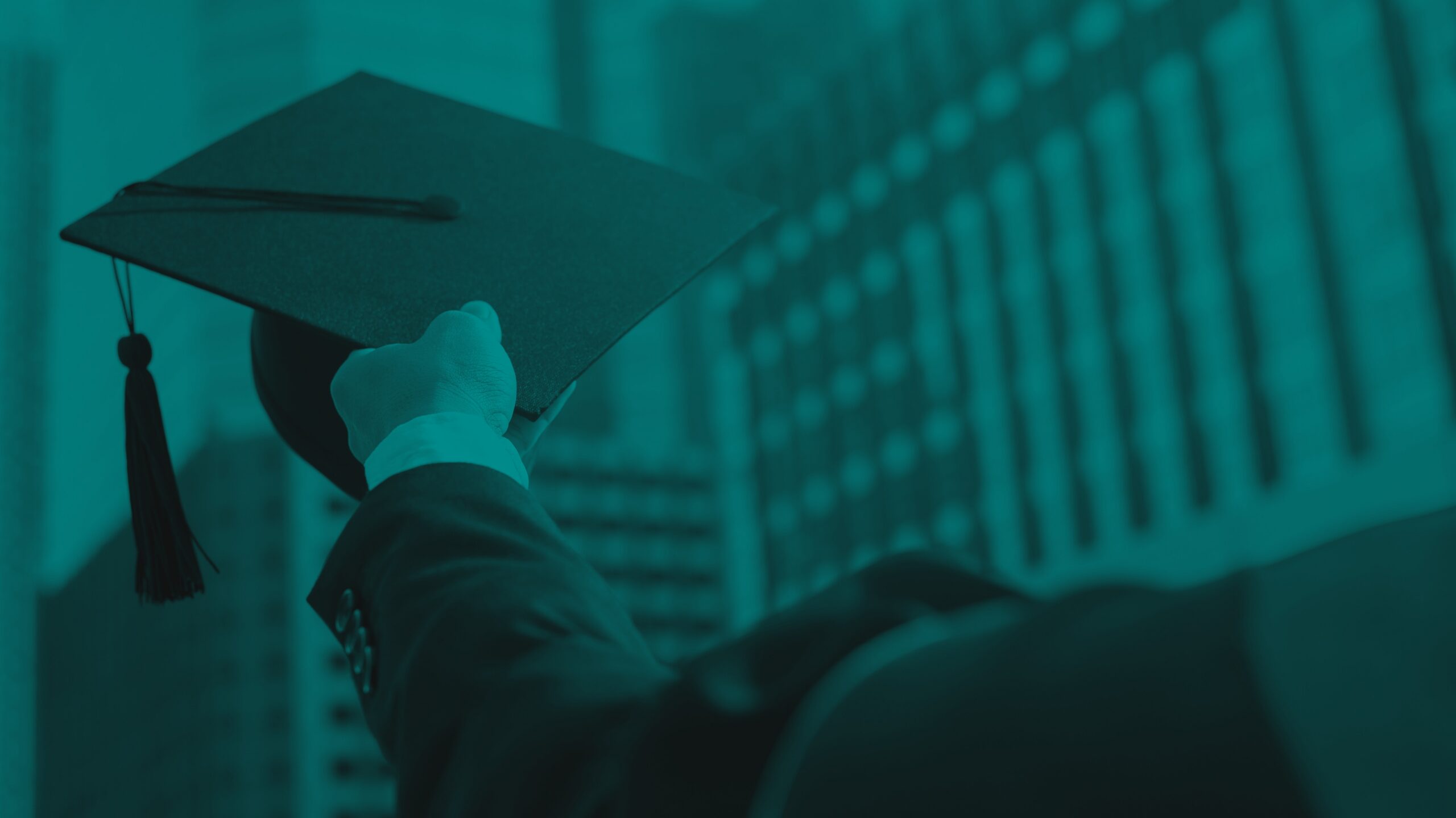 Person holding a graduation cap overhead with a large building in the background.